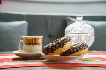 A couple of chocolate donuts on a plate and a cup of coffee.coffee for breakfast
