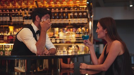 Sitting in smiling beautiful woman guest lively taking with smart bartender while drinking mixed...