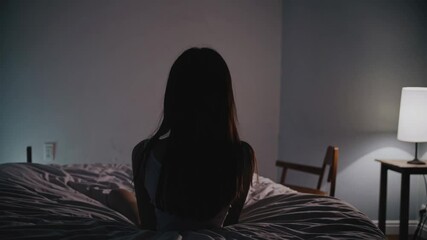 Minimalist bedroom scene with single figure sitting in dim light creates atmospheric mood exploring themes of solitude and personal reflection