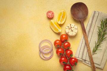 Cherry tomatoes, garlic, lemon slices, carrots, red onions, and rosemary sprig arranged alongside a wooden spoon on a yellow backdrop, culinary creativity and healthy eating concept, copy space