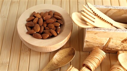 Wooden bowl filled with almonds alongside wooden cutlery set, emphasizing eco-friendly and natural dining choices. Minimalist presentation highlights sustainable lifestyle and natural materials.