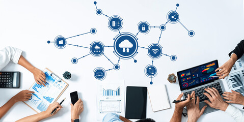 A top-down view of a collaborative workspace showcasing various digital tools and cloud connectivity while team members engage in data analysis and information sharing. Amity