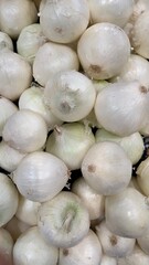 pile of fresh white onions stacked neatly in rustic wooden crate at farmers market bright natural light highlights smooth skins earthy tones create a clean simple organic vegetable display