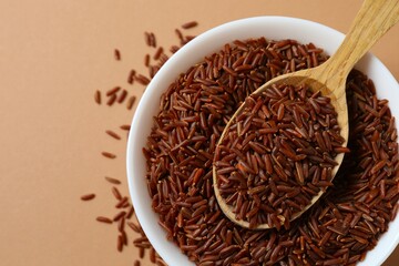 Raw brown rice in bowl on color background