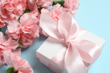 Beautiful bouquet of pink carnations with gift box on a color background