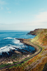 Moody Aerial View of Giant’s Causeway With Waves Crashing Into the Rocks and People Walking Around	