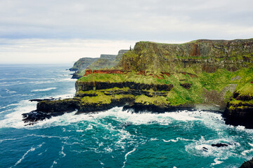 Dramatic Aerial of Giant’s Causeway Cliffs With Crashing Blue Waves During a Cloudy Day