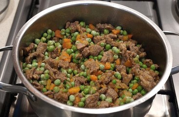 Beef, peas, carrots and spices are cooked slowly in a pot on the stove