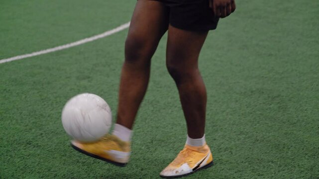 Handheld shot capturing a Black football player in yellow boots showcasing his freestyle skills with the ball on the football field.