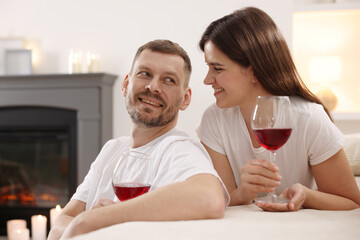 Happy couple with glasses of wine in room with stylish fireplace