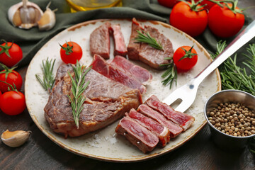 Pieces of delicious beef meat, spices and tomatoes on wooden table, closeup