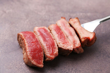 Delicious sliced beef tenderloin with different degrees of doneness on brown textured table, closeup