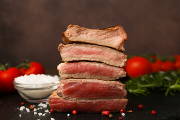 Delicious sliced beef tenderloin with different degrees of doneness and spices on table against brown background, closeup