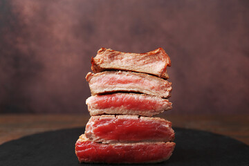 Delicious sliced beef tenderloin with different degrees of doneness on table against brown background, closeup