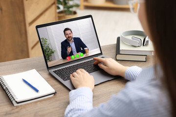 Fototapeta premium Woman listening to speaker via laptop online at table, closeup