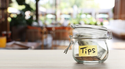Tips jar with money on light wooden table in cafe, space for text. Banner