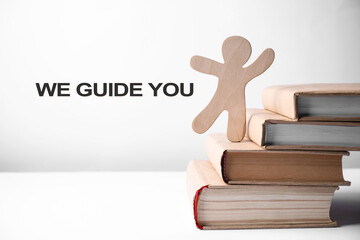 We Guide You text near human wooden figure on books stacked as stairs against white background