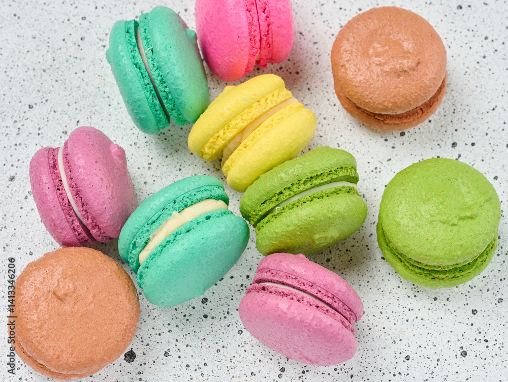 Poster an assortment of colorful macarons on a white surface with dark speckles. the macarons have a smooth