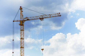 A tall construction crane operates against a cloudy blue sky, showcasing process of building development. Construction and industrial industrial.