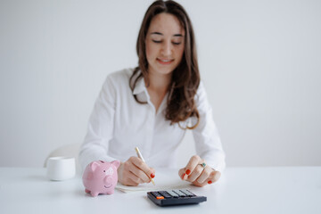 Woman calculating expenses with piggy bank and calculator in a bright workspace during daytime