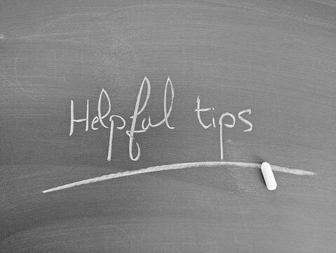 Chalkboard with the words: "Helpful Tips". A chalk stick rests on the board. Education concept for learning something new.