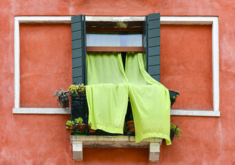 Detail of the exterior of an orange house with lime-green curtains and succulent plants on a small balcony, Venice, Veneto, Italy
