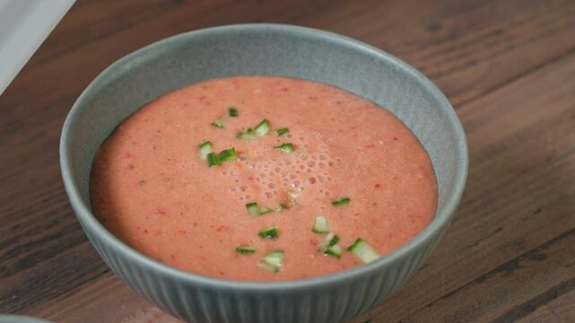 cook add chopped vegetables in a bowl of gazpacho, process of making fresh cold tomato soup. food closeup