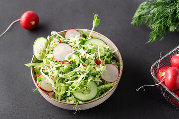 Diet low carb spring salad with juice cabbage, cucumbers, dill, parsley, green onion, small radish and olive oil on black stone table close up.