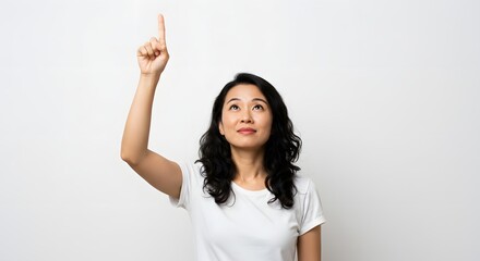 An attractive Asian woman gestures upwards, pointing her finger towards something unseen with a white backdrop.