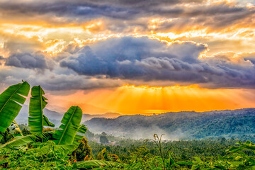 Coastal valley, Bali, Indonesia. Sun breaking through clouds over a lush valley at sunset.