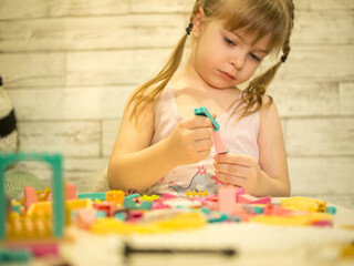 A young teenage girl assembles a construction set from plastic parts and blocks with her hands.