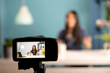 Asian content creator sitting at desk, holding a cup of coffee, speaking into a microphone. Digital...