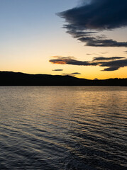 Fototapeta premium A calm lake reflects the rich colors of sunset as the blue hour envelops the landscape. Dark silhouettes of mountains rise against the vibrant sky in Dalarna, Sweden