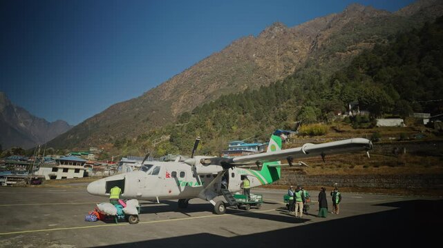 Airport staff handling baggage beside small aircraft at Lukla mountainside airstrip of Tenzing Hillary Airport, Lukla, Nepal