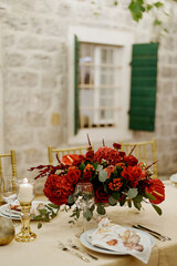 Red bouquet of flowers stands on a festive table in the courtyard of an old house with green shutters