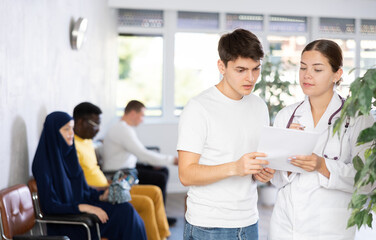 Dissatisfied surprised young man discussing documents with a doctor in the lobby of a medical clinic