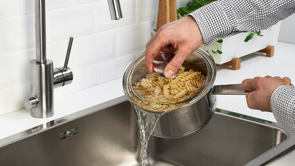 Cooking pasta in a modern kitchen while draining water in a stainless steel sink.