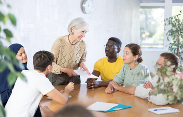 Obraz premium Round table meeting - senior female manager conducts training for employees of different nationalities