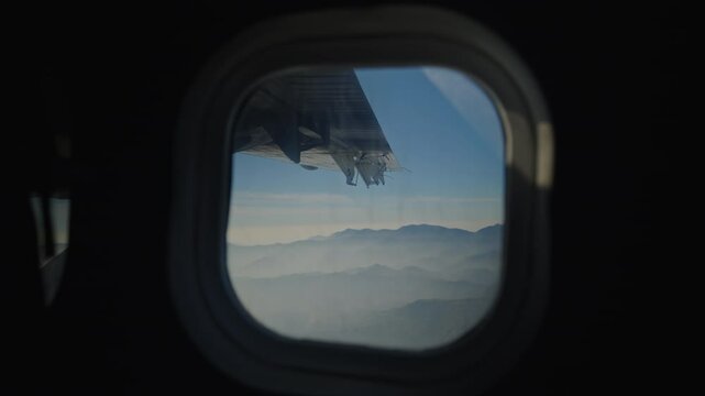 Airplane wing soaring above snow capped Himalayan peaks through the passenger window, revealing dramatic mountain wilderness of Nepal's rugged terrain