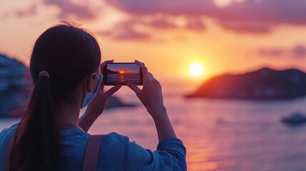 Asian female capturing sunset over ocean with smartphone on serene evening