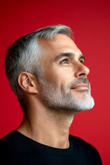 Obraz premium A trendy man showcasing a fashionable hairstyle. Elegant men's crew cut haircut - midlife white man with grey hair. Red solid background. Conceptual art of style for aging men.