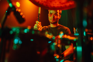 Drummer playing drums during live performance on stage with colorful lighting