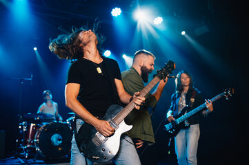 Rock band performing energetically on stage under blue lights