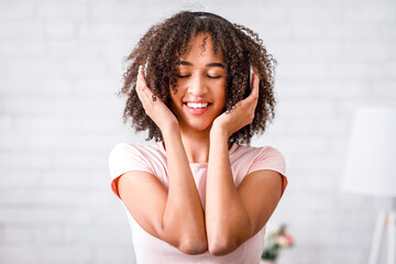 Happy moments with music at home. African american woman with closed eyes and headphones in living...