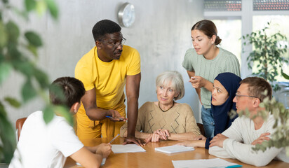 Adult African American male tutor conducting lesson for group of interested adult people of...