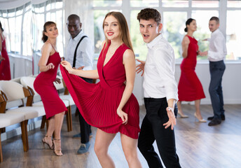 Fototapeta premium Group of young contemporary active people practicing vogue dancing movements while training twist or charleston in dance hall
