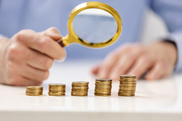 Analyzing stacked coins with a magnifying glass in a financial setting