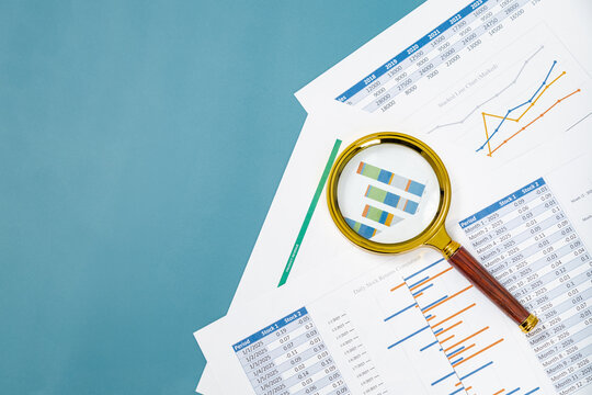 Analysis of financial data with charts and graphs under a magnifying glass on a blue background - Powered by Adobe