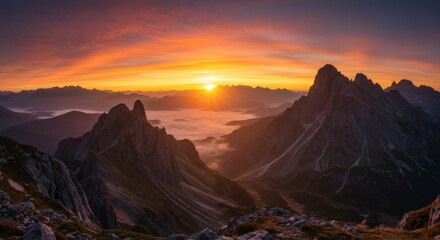 Naklejka premium A stunning panorama of mountain peaks under a brilliant sunrise, with an orange sky and fog below.