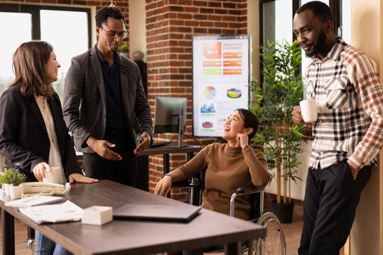 Multiracial professionals in a creative startup office taking a moment to unwind, chatting and laughing together during a break. African american man with glasses, sharing a story to his team.